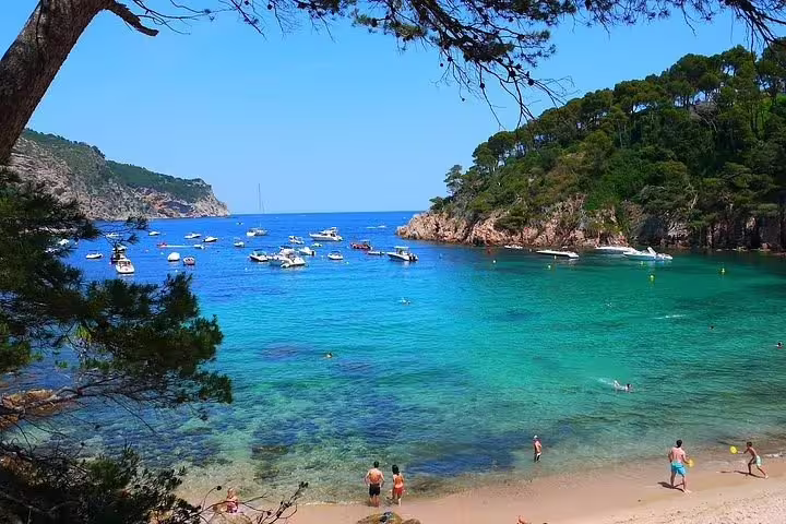 Idyllic beach scene on Costa Brava with clear blue waters and boats, highlighting the allure of the Girona City tour.