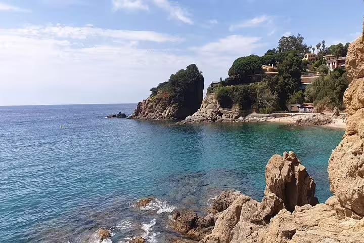 Scenic Costa Brava coastline with crystal-clear waters and rugged cliffs under a blue sky.