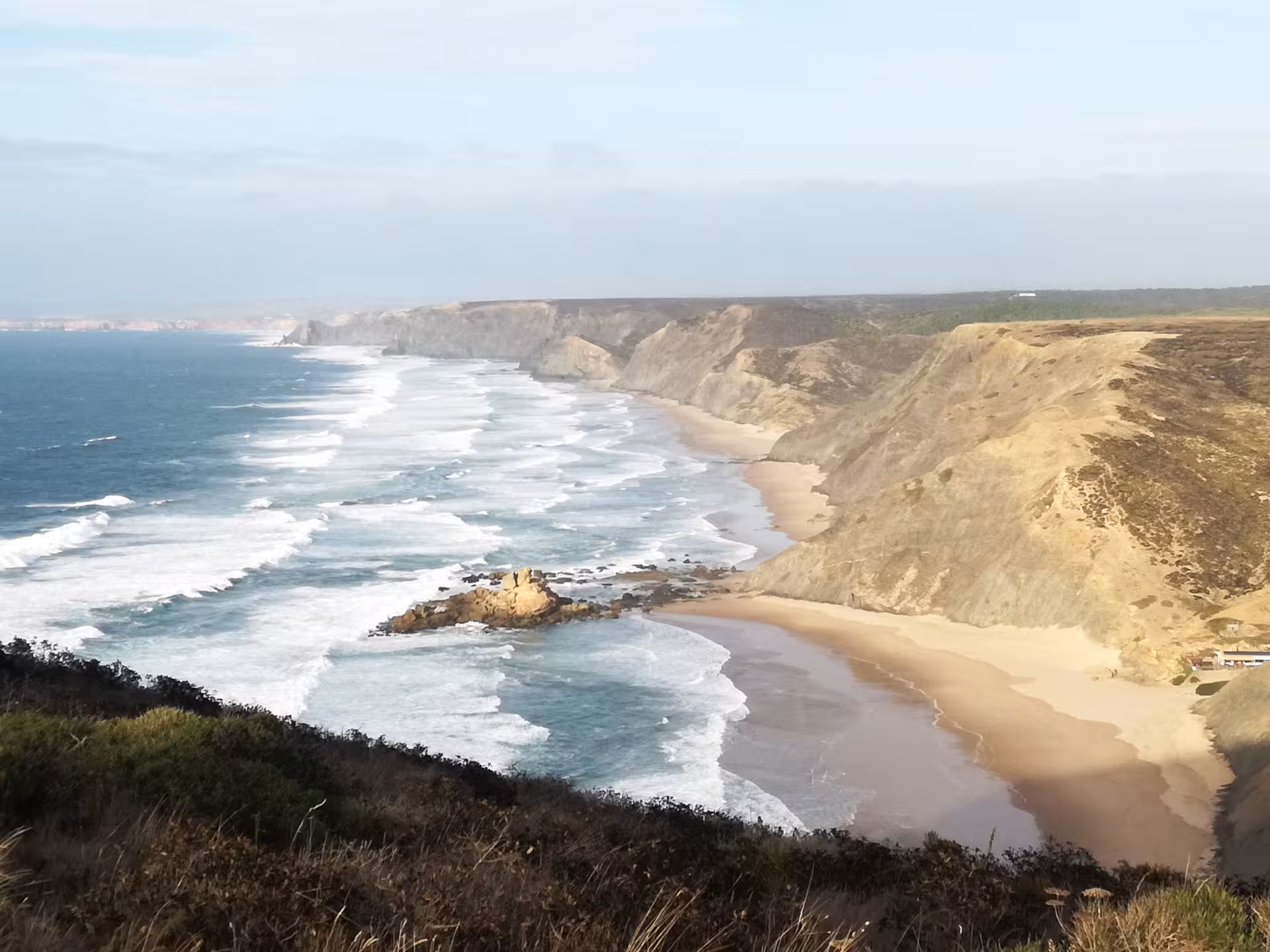 Sweeping view of golden cliffs, empty sandy beach and rolling Atlantic surf along Portugal’s remote Costa Vicentina wild coast