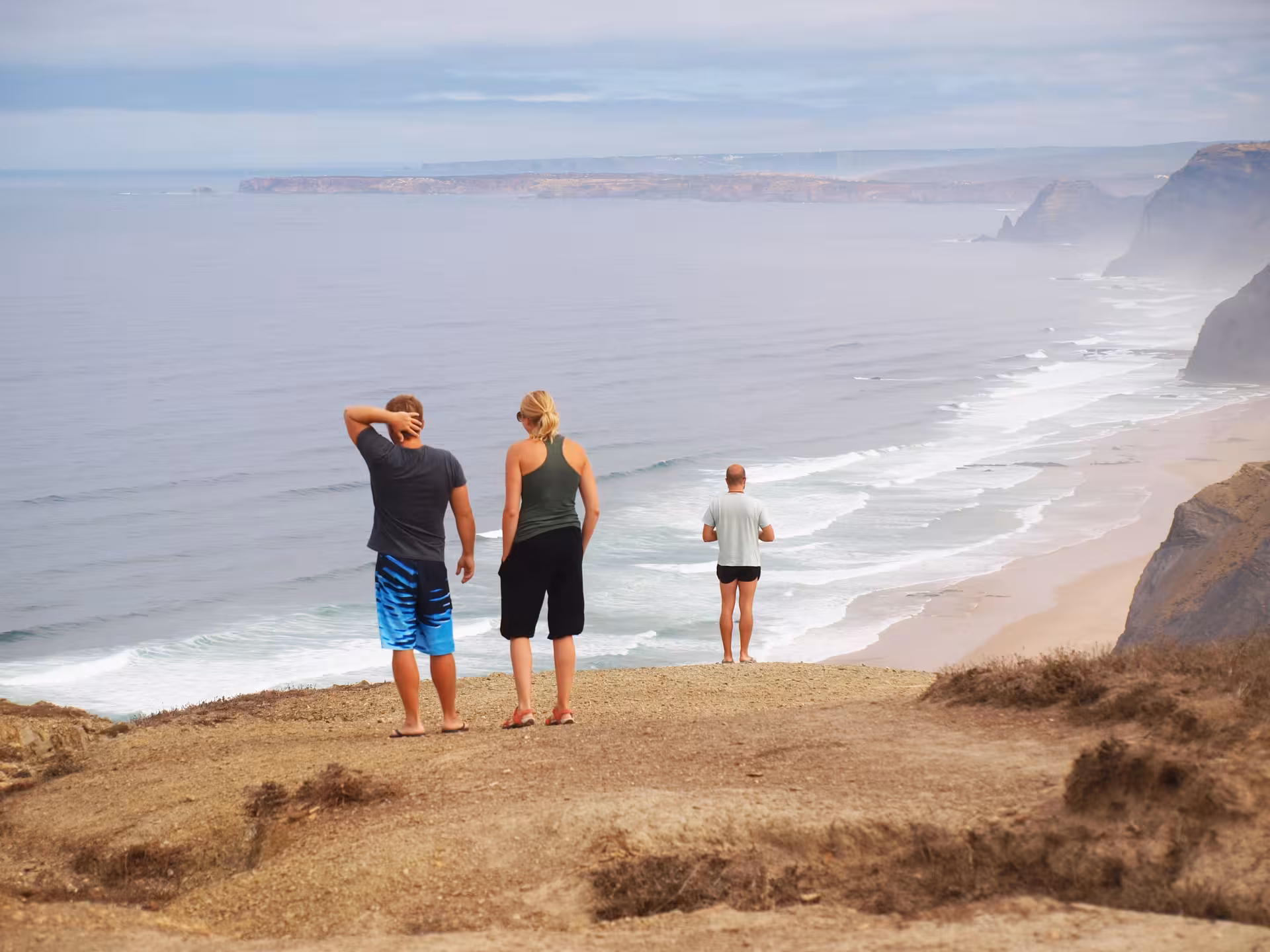 Small group of hikers standing on a cliff edge overlooking misty beaches and surf on Portugal’s Costa Vicentina wild coast