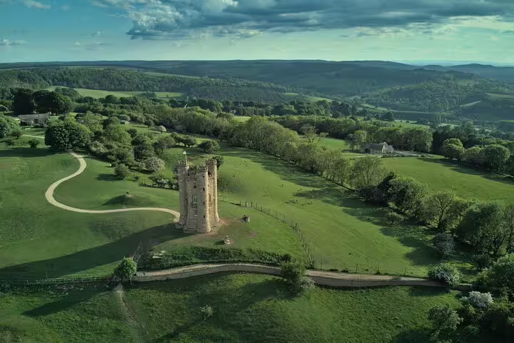 Rolling Cotswolds countryside with historic tower and green hills, scenic stop on a day trip from London