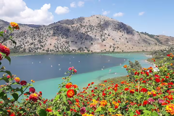Vibrant flowers overlooking a tranquil turquoise lake against a backdrop of rugged hills in Crete.