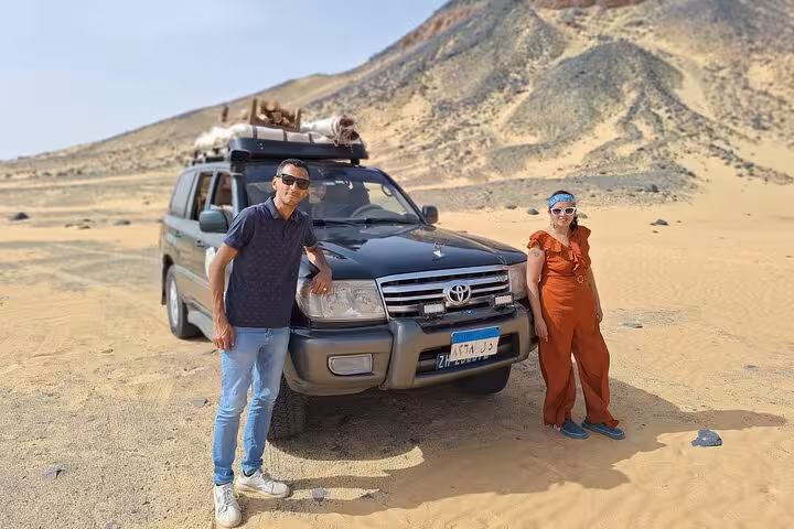 Couple stands beside a 4x4 vehicle ready for an adventurous ride through the scenic Black Desert terrain.