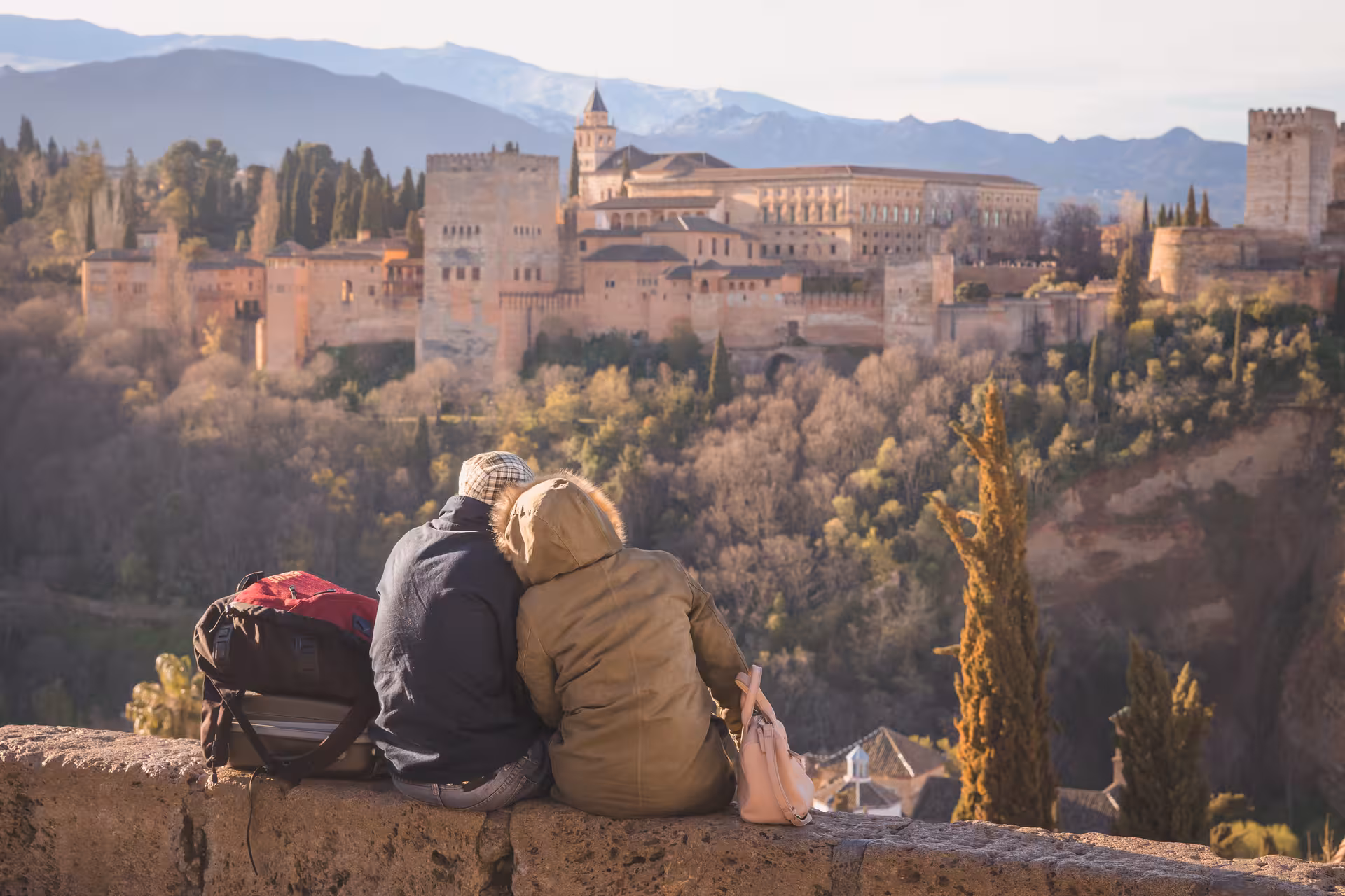 Couple enjoying a panoramic view of the Alhambra from Albaicín, surrounded by lush trees and mountains.