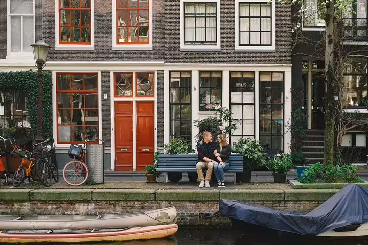 Couple on bench by Amsterdam canal houses and bicycles, perfect for personal travel photographer tour photoshoot