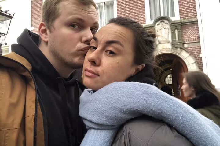 Couple posing together during Amsterdam canal walking tour with historic brick building in background