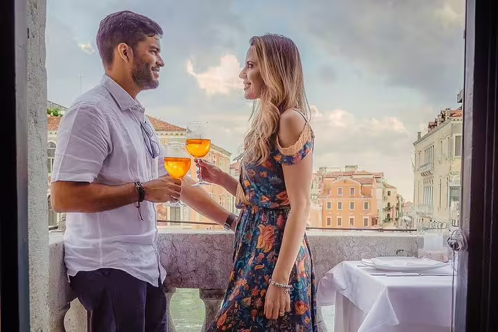 Couple enjoying aperitifs on a Venetian palace balcony, overlooking canals, perfect for a romantic gondola tour booking.