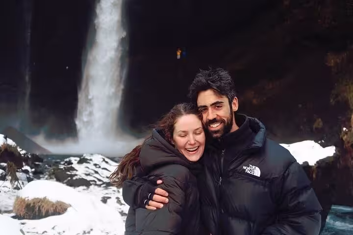 Couple laughing in front of a snowy waterfall on Iceland's South Coast