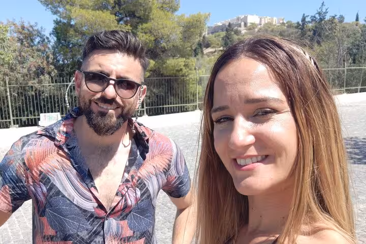 Couple smiling on Athens walking tour with Acropolis visible on hill in background