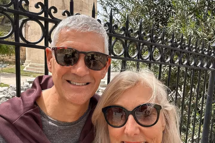 Smiling couple wearing sunglasses posing in front of ornate iron gate in Athens, Greece