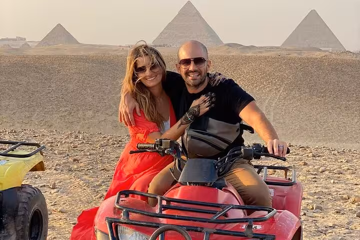 Couple on ATV quad bike in Giza desert with pyramids behind, part of private tour with camel ride and dinner cruise