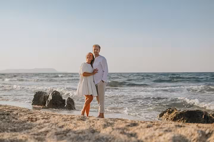 Smiling couple embracing on a sandy beach with waves in Agios Nikolaos, perfect for a private photoshoot experience.