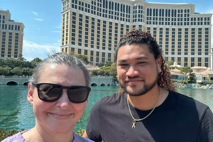 Two visitors smiling in front of the Bellagio hotel and fountains on the Las Vegas Strip