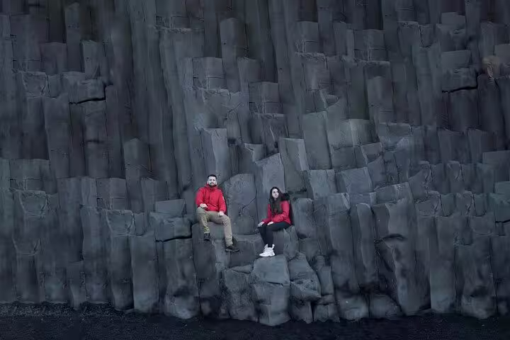 Couple in red jackets sitting on black basalt rock columns on Iceland's south coast