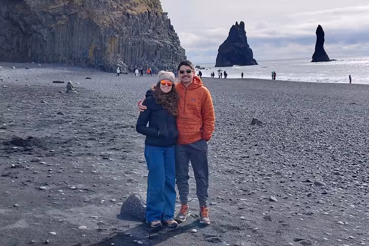 Couple posing on black sand beach with volcanic rock stacks on Iceland's South Coast