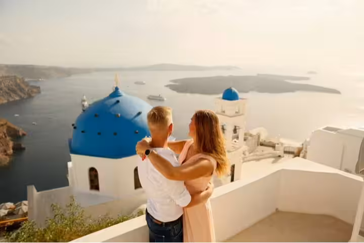 Couple embraces overlooking iconic blue domes of Santorini, capturing unforgettable vacation memories with a photographer.