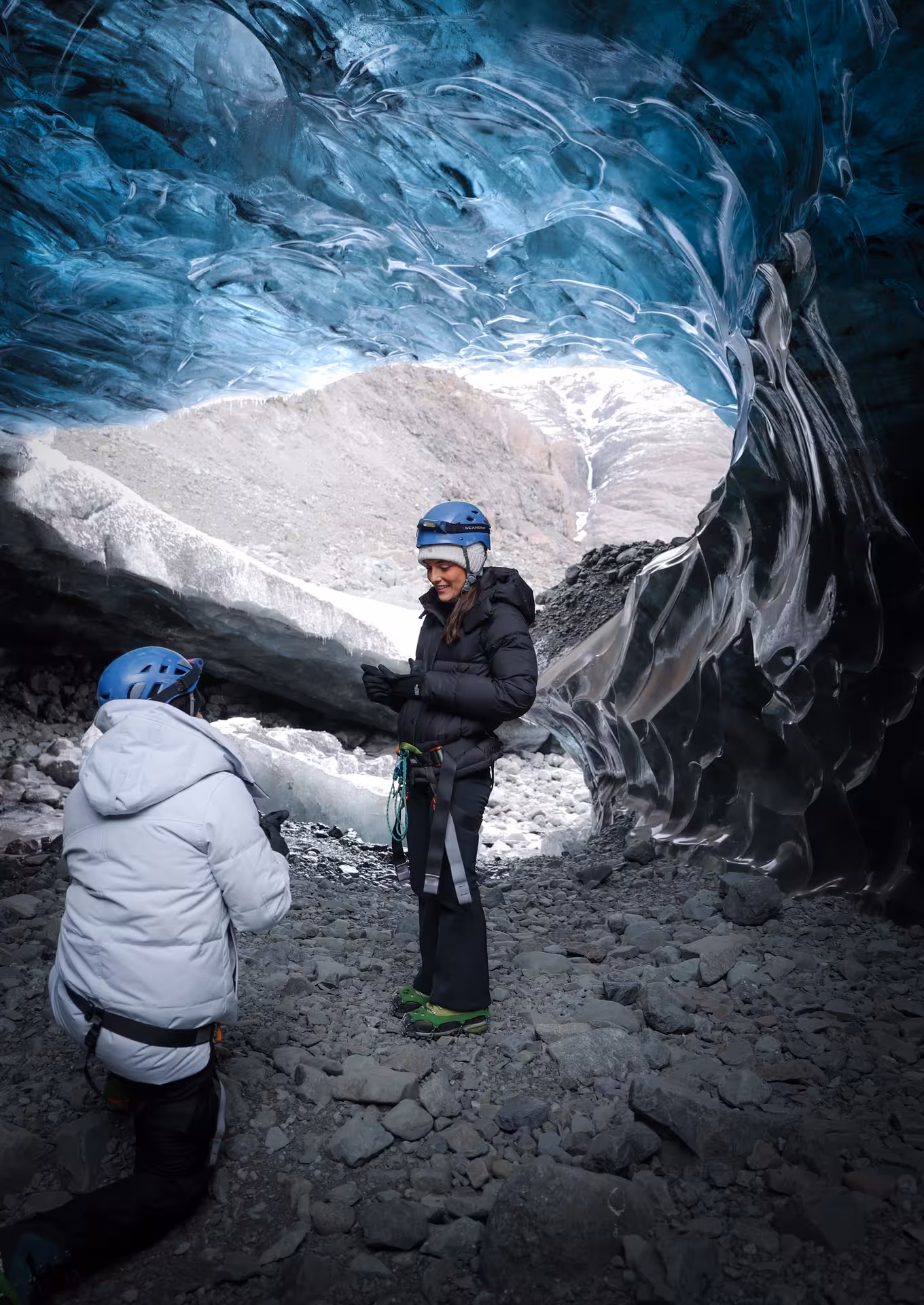 Couple exploring stunning blue ice cave on Iceland glacier lagoon proposal tour wearing helmets and winter gear
