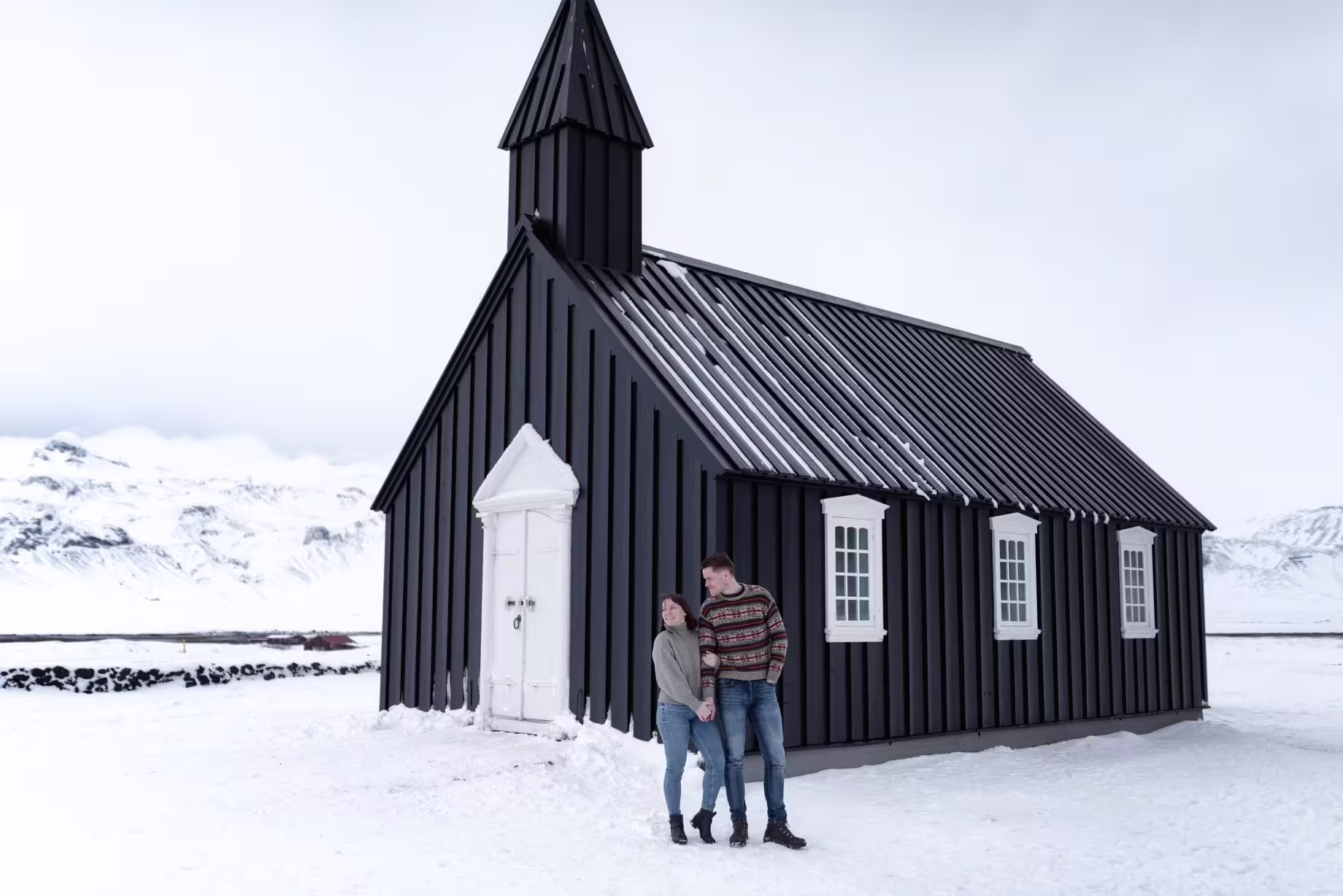 Couple posing at the iconic black Budakirkja church in snow on a Snaefellsnes west Iceland tour