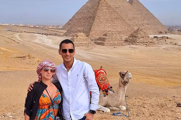 Couple posing with a camel against the stunning backdrop of the Pyramids of Giza on a private guided tour.