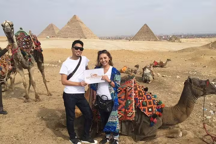 Couple posing by camels at the Pyramids of Giza, popular sunrise or sunset tour with camel ride experience