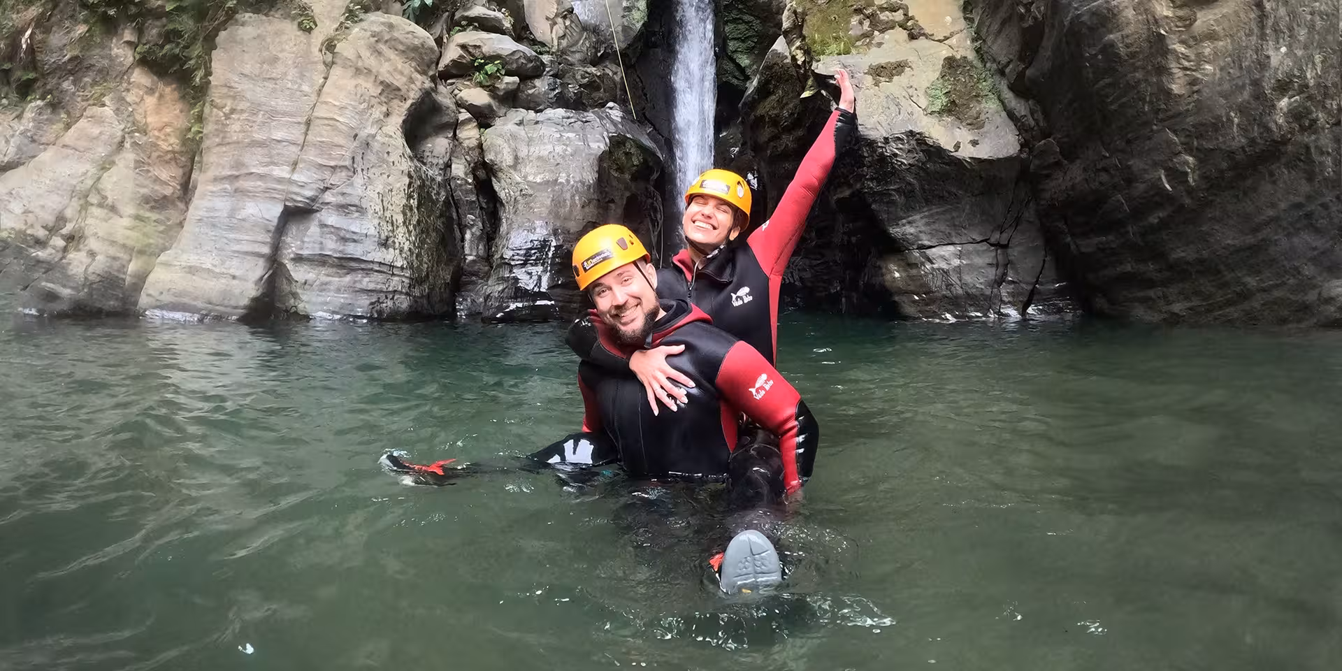 Couple in wetsuits swimming in pool below Salto do Cabrito waterfall, São Miguel Azores canyoning tour