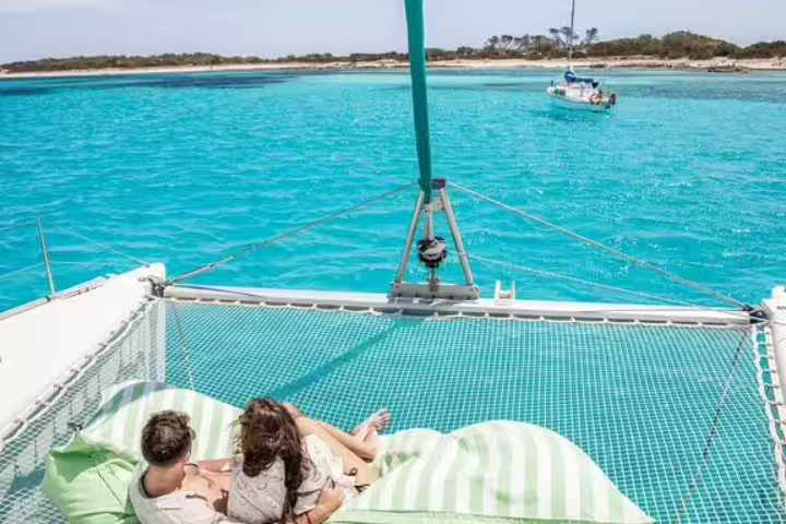 Couple relaxing on a catamaran net over turquoise waters during a Formentera and Ibiza small group sailing trip.