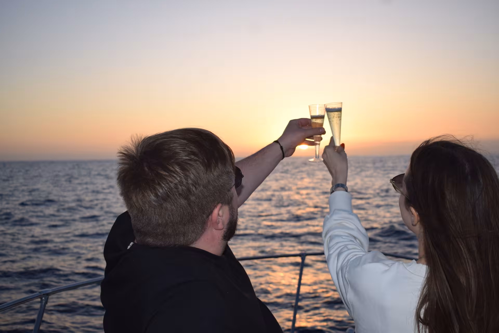 Couple toasting champagne glasses on a private sunset cruise with stunning ocean views, perfect for a romantic getaway.