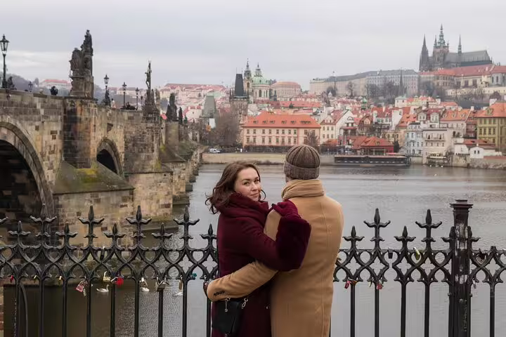 Couple embraces by the iconic Charles Bridge with Prague Castle in the background during a professional photoshoot.
