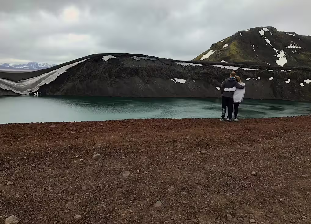 Couple embracing overlooking turquoise crater lake at Landmannalaugar highlands Iceland
