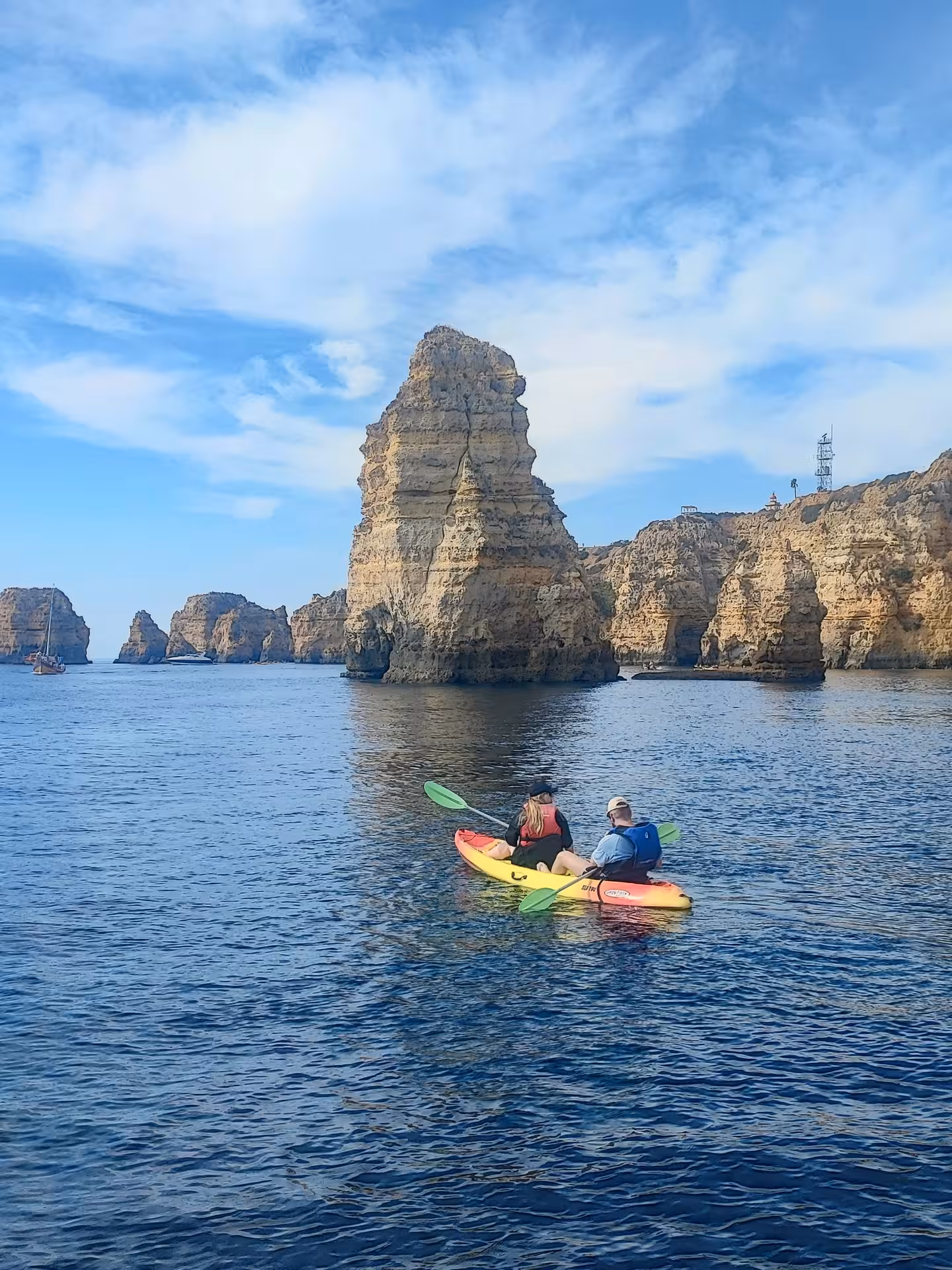 Couple paddling a double kayak along Algarve’s dramatic sea cliffs and rock stacks on a calm, sunny ocean tour