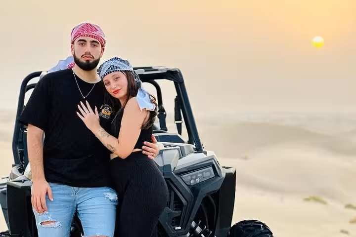 Couple posing by dune buggy in desert at sunset, ready for quad bike adventure and thrilling dune bashing ride