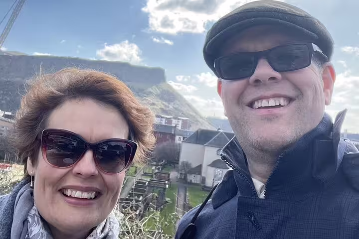 Smiling couple on Edinburgh self-guided walking tour with historic buildings and Arthur's Seat in background