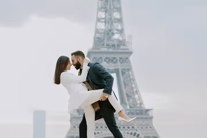 Couple embracing in front of the Eiffel Tower in Paris, man lifting woman in white outfit