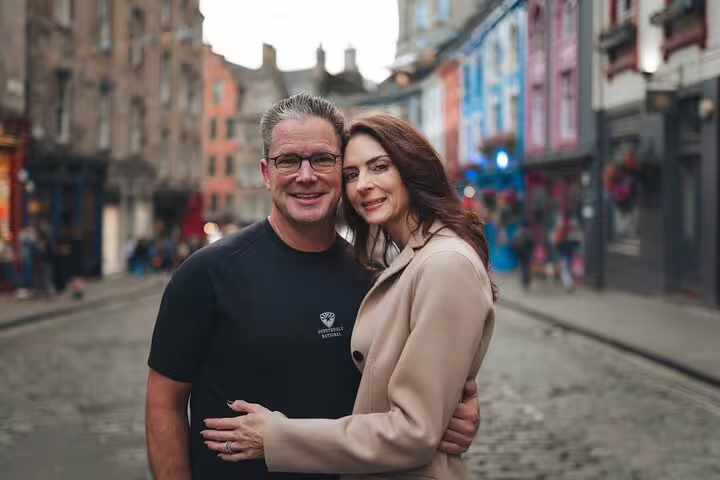 Couple embraces on a historic cobblestone street lined with colorful buildings in Edinburgh's Old Town.
