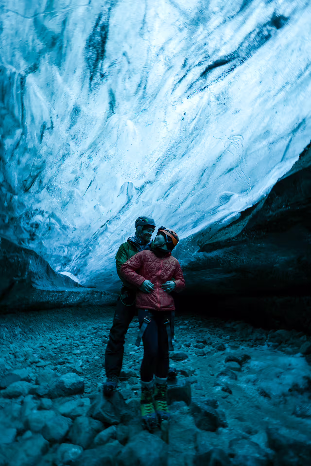 A couple in helmets and winter gear embracing inside a stunning blue Iceland glacier ice cave tour