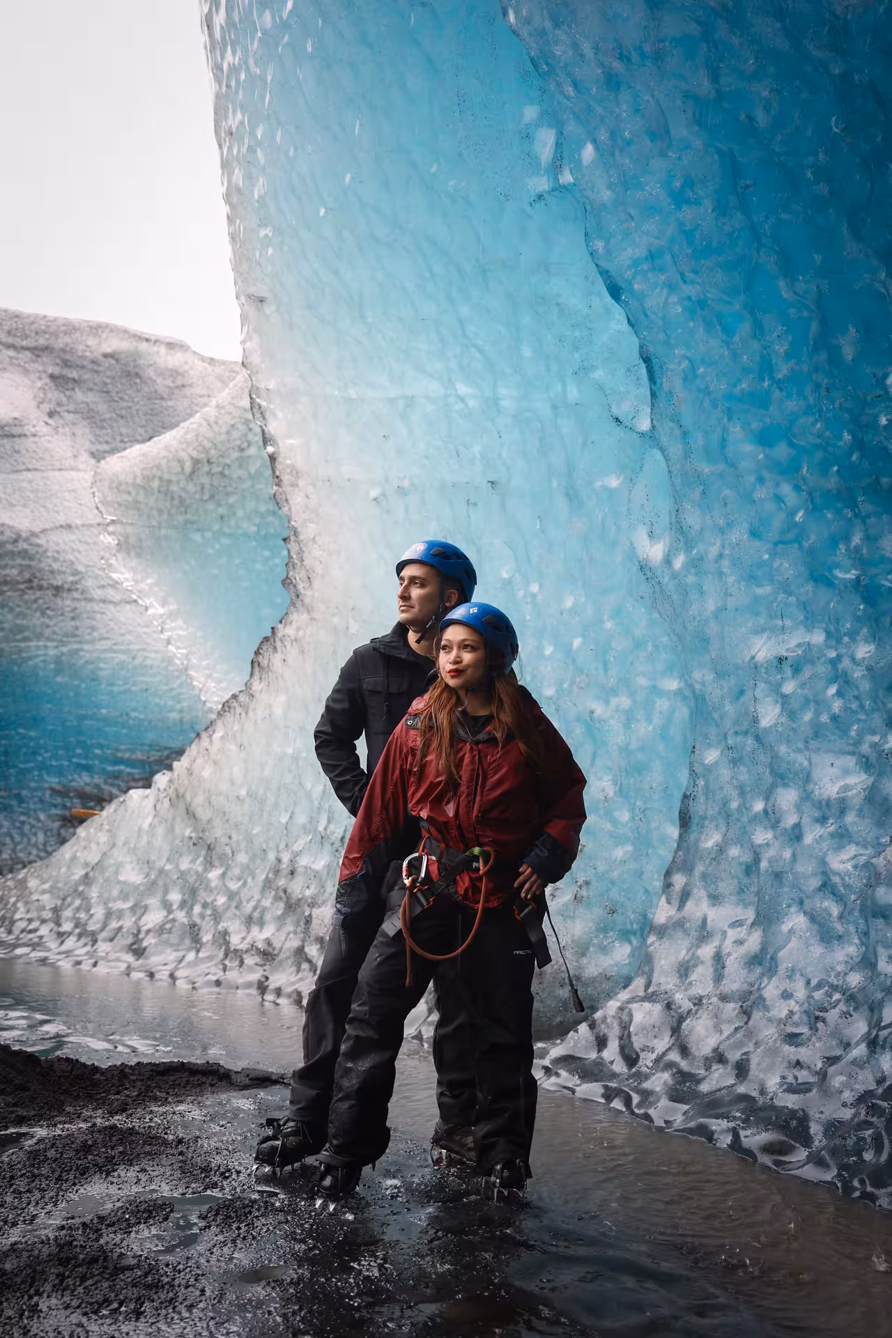 Couple in helmets and gear exploring a stunning blue glacier wall on an Iceland sunrise proposal tour with Glacier Lagoon.