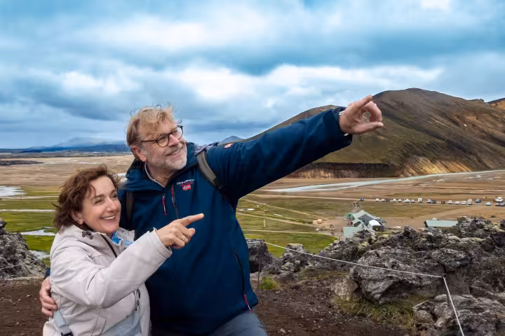 Couple pointing at Iceland highland landscape with colorful mountains and camping area below on guided tour