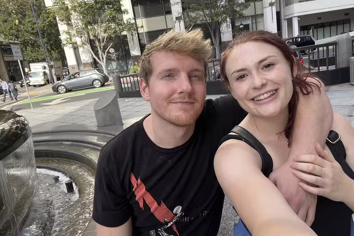 Couple smiling together near a fountain in an urban plaza during a walking tour