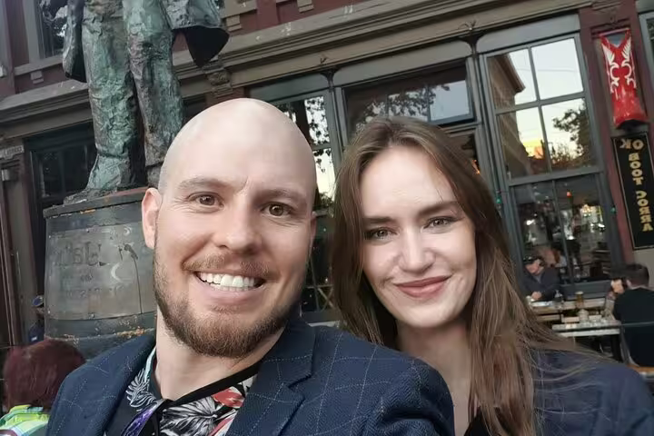 Couple smiling in front of bronze statue at Gastown Vancouver during walking tour
