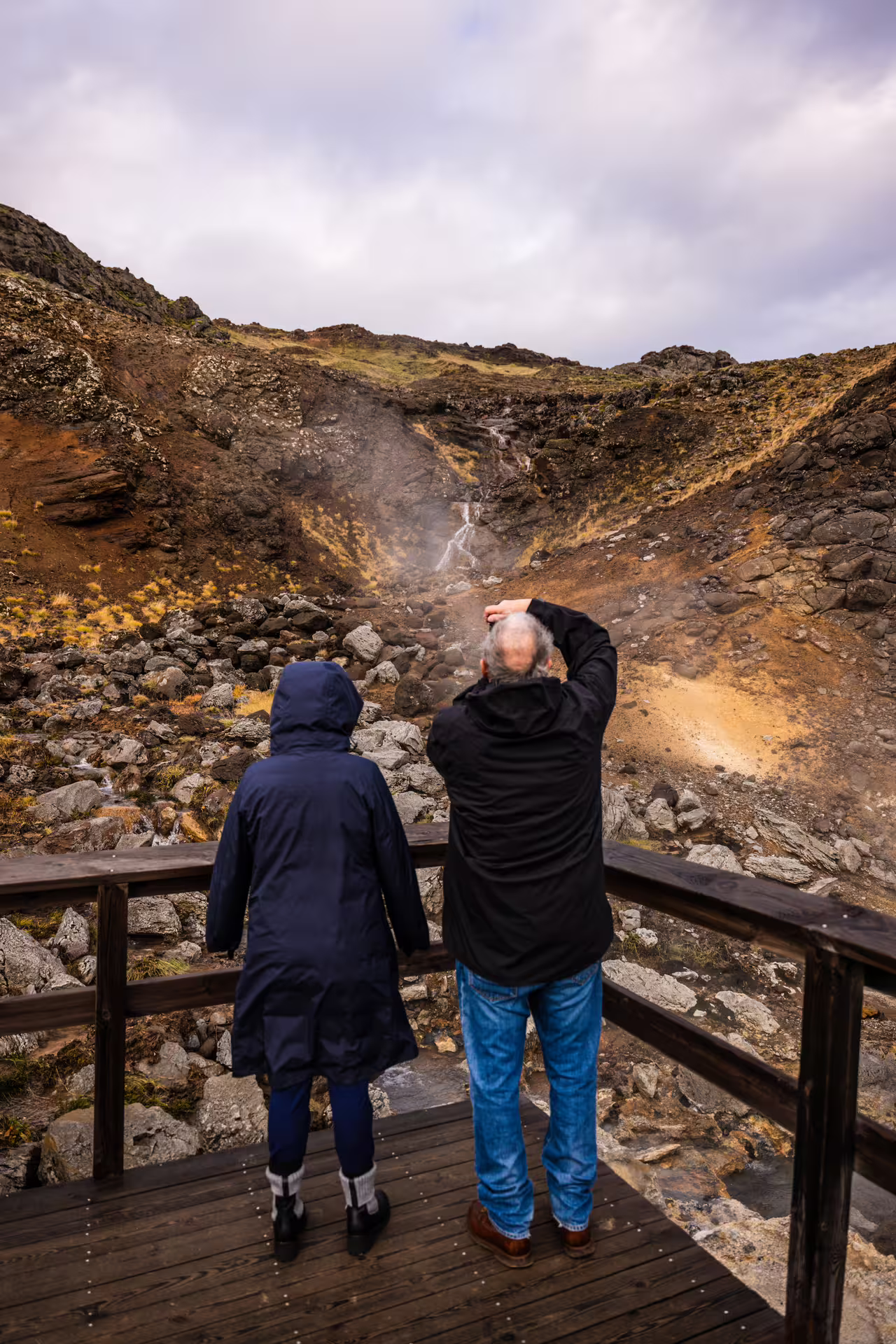 Couple photographing a steaming geothermal waterfall in a volcanic canyon on a Reykjanes Peninsula day trip Iceland