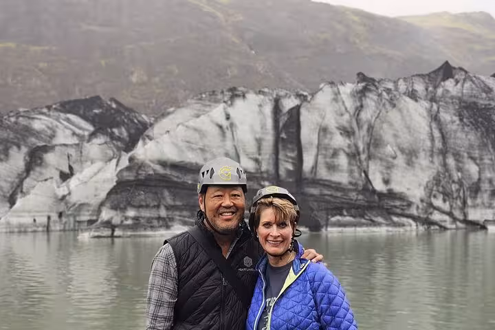 Couple wearing helmets smiling in front of a glacier and glacial lake on Iceland's South Coast