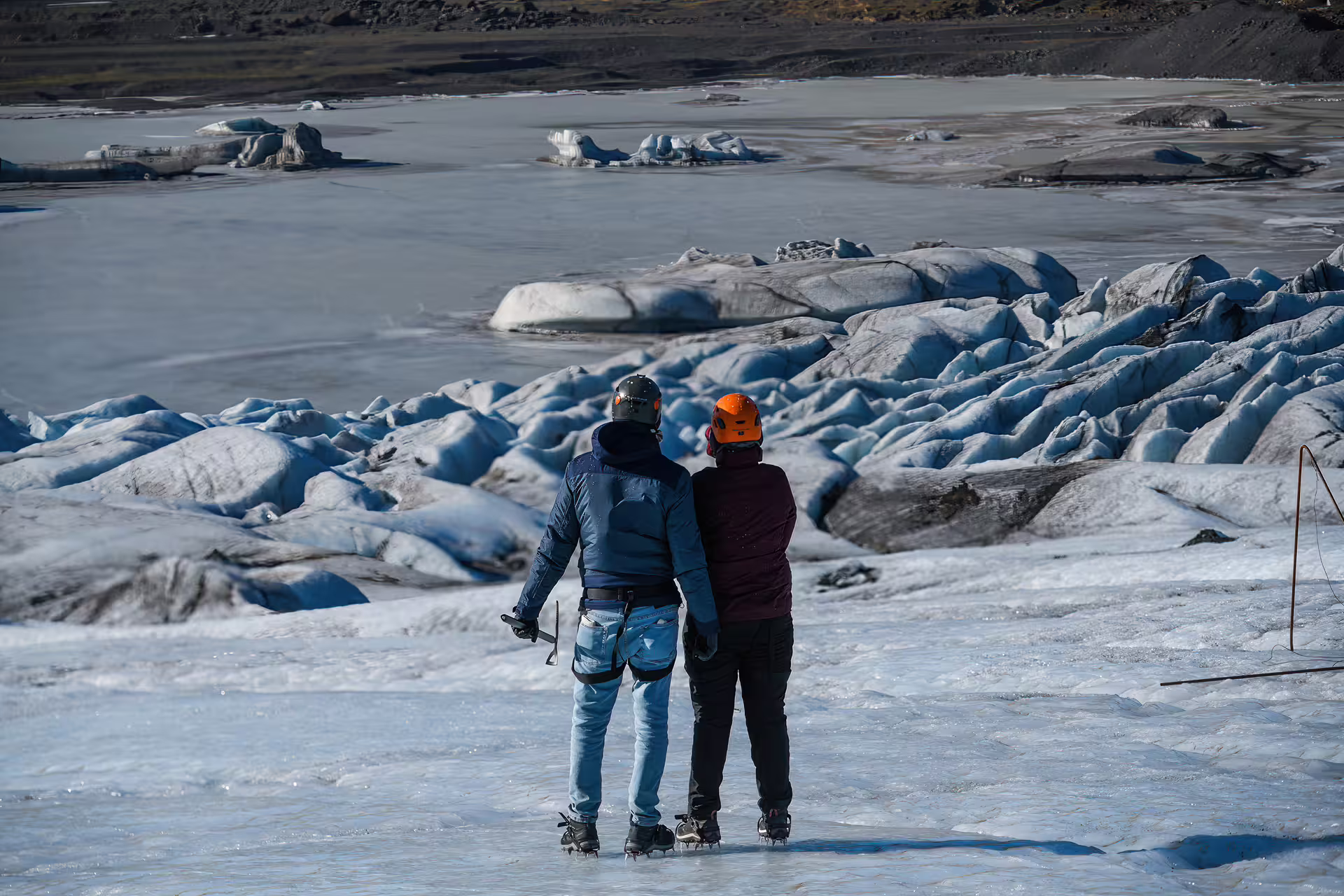 Couple in helmets and crampons admiring stunning glacier lagoon views on Iceland South Coast glacier hike adventure