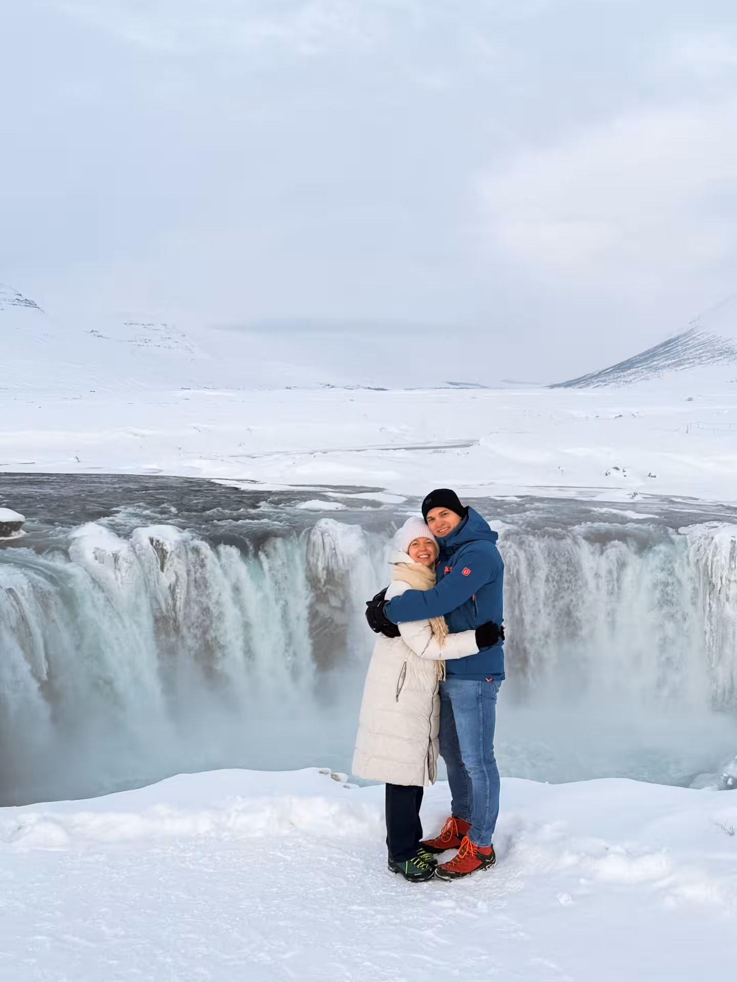 Couple posing at snowy Goðafoss Waterfall viewpoint, North Iceland, on Northern Wonders adventure day tour