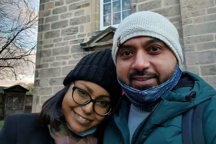 Couple in winter hats and face masks posing in front of a historic stone building in Edinburgh
