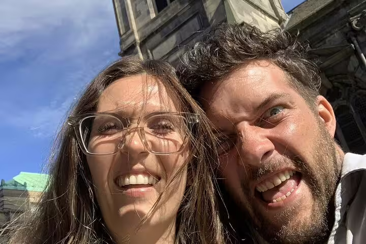 Couple smiling on self-guided Gothic mystery walking tour in Edinburgh with historic building behind