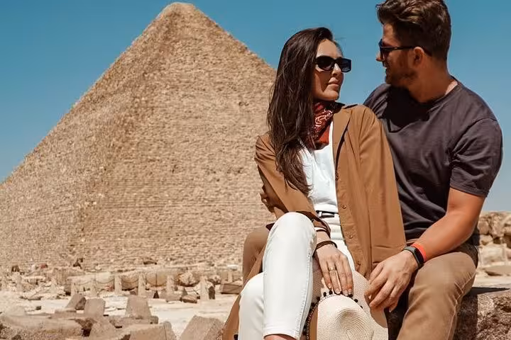 Couple sitting near the Great Pyramid of Giza during a half-day guided Giza Pyramids and Sphinx tour with lunch