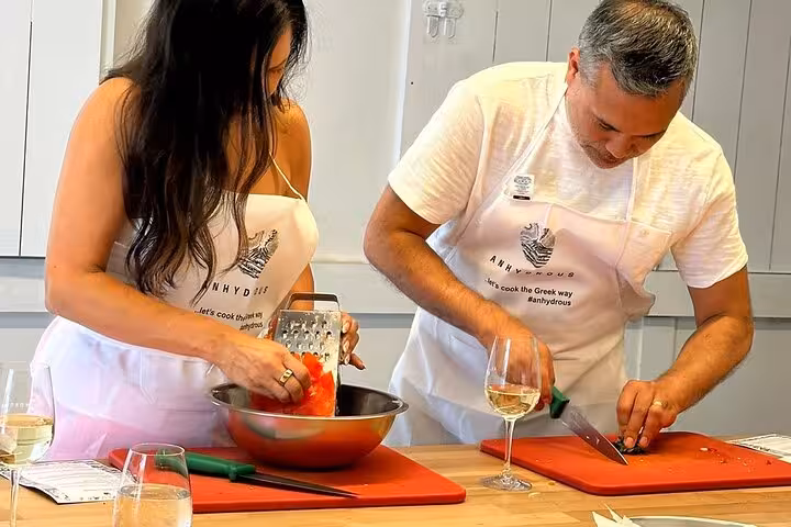 Couple prepping Greek meze in a Santorini private cooking class with local wine, included in island tour experience