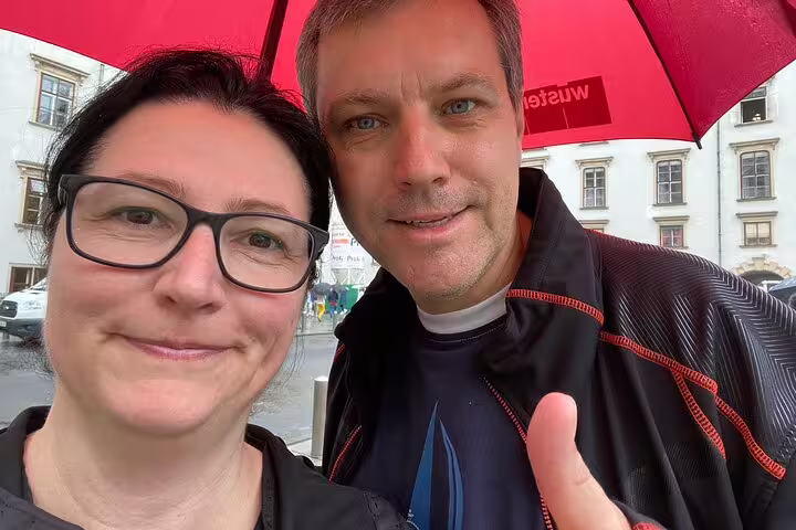 Two smiling tourists sharing a red umbrella on a rainy day in Vienna's historic city center