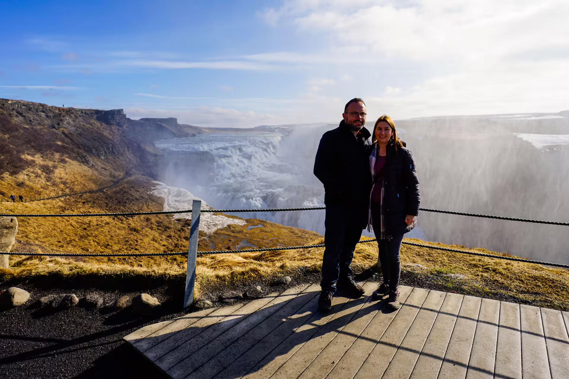 Couple enjoying the stunning view of Gullfoss waterfall on a sunny day during Golden Circle tour in Iceland.