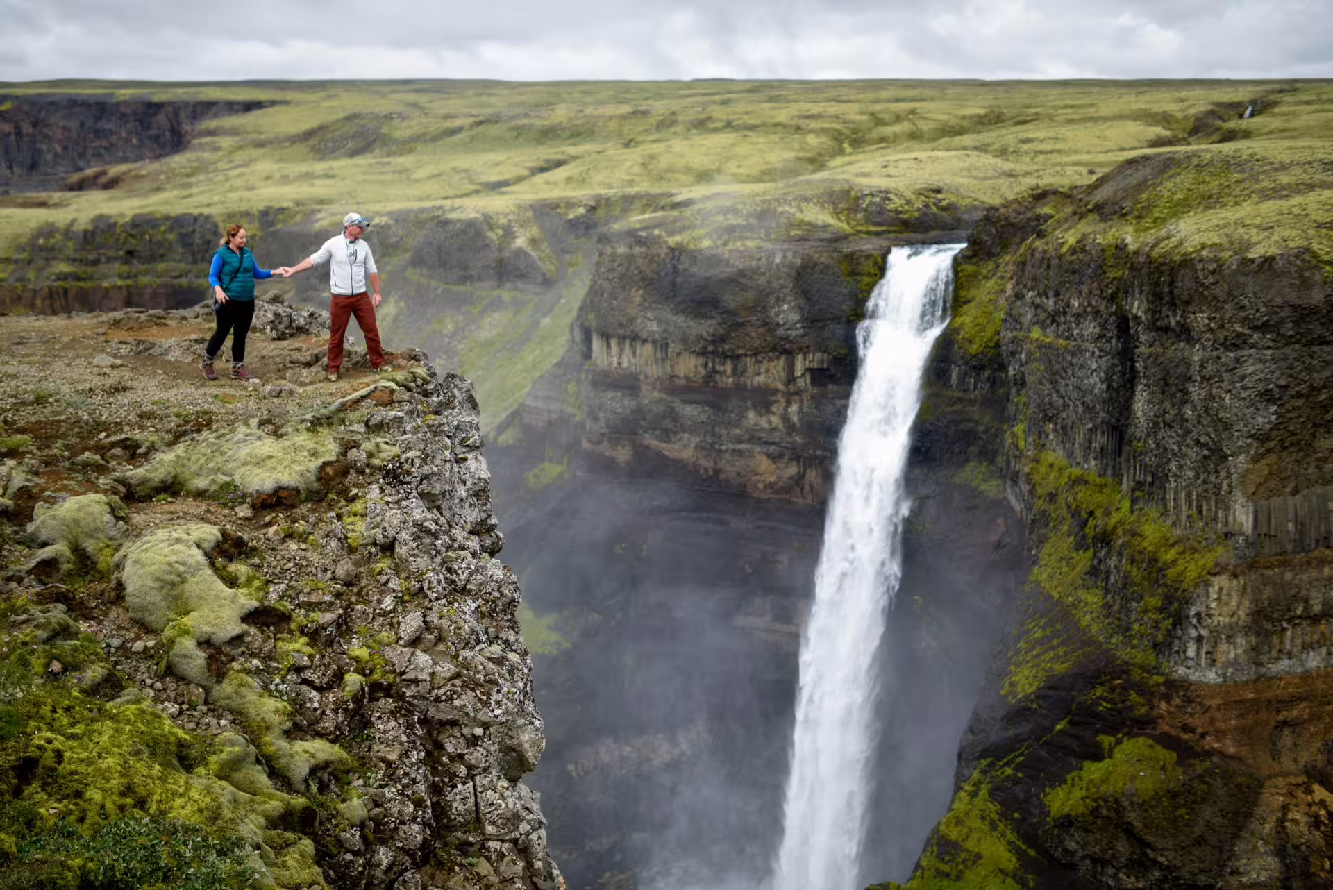 Couple holding hands at the edge of Haifoss waterfall cliff on an Iceland grand tour hiking excursion